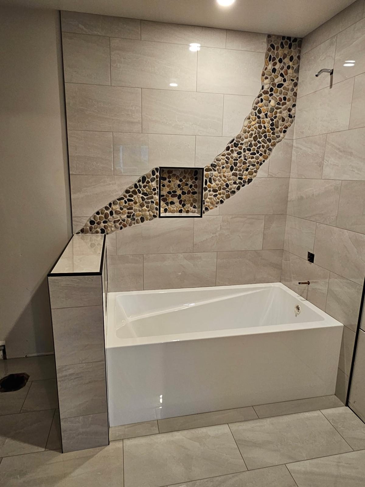 Soaker tub with a curved pebble mosaic feature wall and built-in niche
